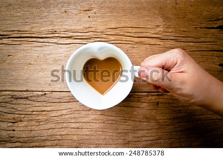 Valentine Day Concept and Idea. Hand Holding Drinking, Coffee Mug in Design of Heart Shape, Love and romantic idea on Wood Table Background, Food Rustic Still Life Style.