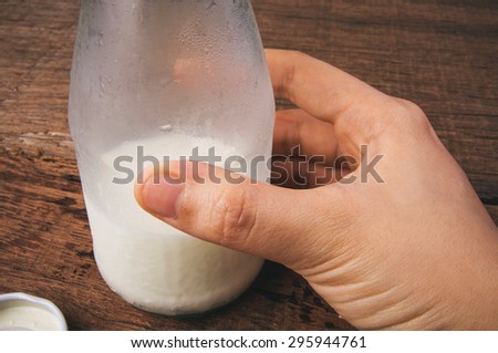 Fresh Milk, Glasses Bottle Opened with Hand Holding. Ready to Drink, Organic Dairy Produce, Concept and Idea of Breakfast on Wood Table Background, Country Rustic Still Life Style. Close up.