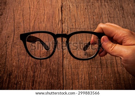 Eyeglasses, Clear Glasses, Black Frame Fashion Vintage Style, Hand Holding  on Wood Desk Background, Rustic Still Life Style.