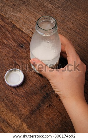 Fresh Milk, Glasses Bottle Opened with Hand Holding. Ready to Drink, Organic Dairy Produce. Wood Table Background, Country Rustic Still Life Style. Vertical.