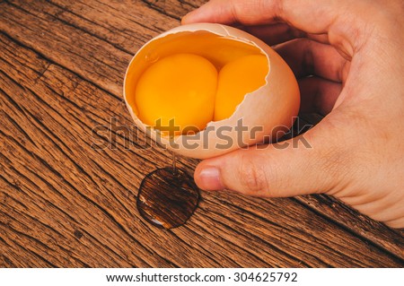 Double Yolks, Fresh Twin Egg Yolks in Egg Shell with Hand Holding on Wood Table Background, Country Rustic Style. Concept Idea of Cooking and Baking.