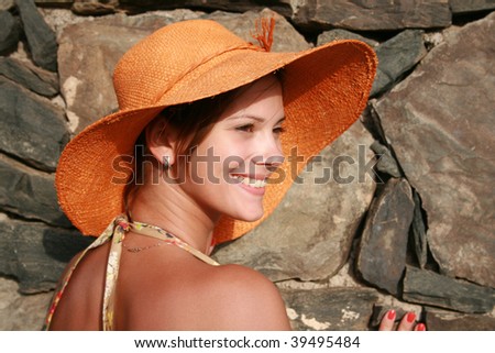 Woman in orange hat posing near with stone wall