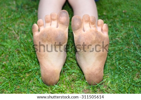 Dirty muddy child\'s soles of the feet against green grass