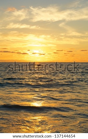 Vertical photo of a small water craft or boat on the waters of the Pacific Ocean at sunset