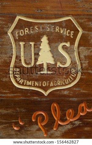 Distressed wooden sign with carved US Forest Service and Department of Agriculture logo at a camp site.