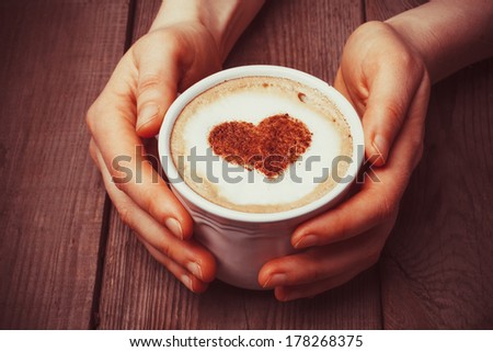 Hands holding a cup of coffee with heart on foam