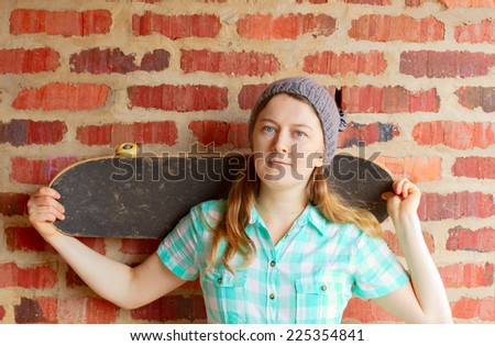 Woman holding skateboard against brick wall