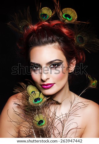 Woman with  peacock hair styling, bright make up holding peacocks feathers