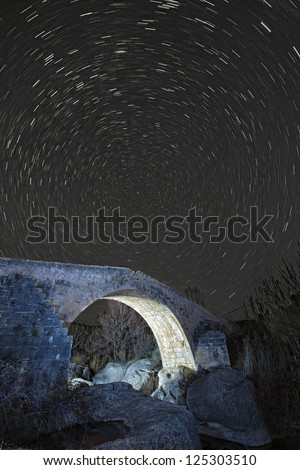 roman bridge at night with star trails in the sky.Star movement is caused by Earth\'s rotation and camera\'s long exposure.