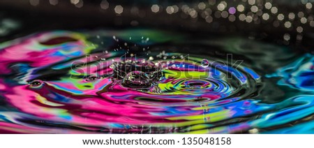 Water splash and waves in multiple colors with a bubble of water flying to the side against a de-focused background