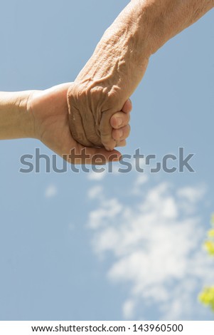 A senior and women holding hands under a blue sky with clouds A senior and women holding hands under a blue sky with clouds
