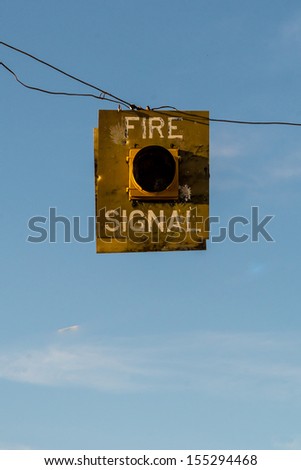 An antique fire signal hanging from a wire with a blue sky background