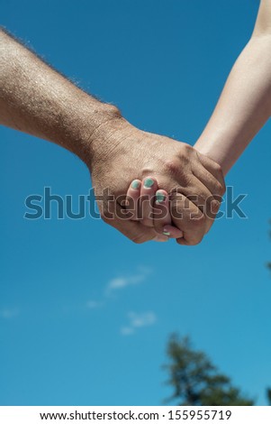 A young female person holding hands with an older male person close up outdoors