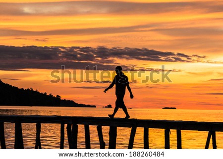 A man, only seen as a silhouette, walking on a jetty at sunset on a remote island (Togian) in Sulawesi, Indonesia