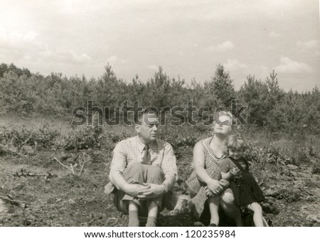 Vintage photo of parents with little daughter resting outdoor (fifties)
