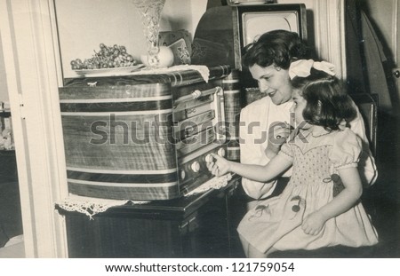 PARIS,FRANCE, CIRCA 1955 -vintage photo of mother and daughter listening to old fashioned radio, Paris, France, circa 1955