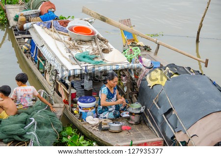 CHAU DOC, VIETNAM - JANUARY 2: Unidentified fisherman's wife cooks a meal on her wooden boat while her children are resting near her on January 2, 2013, in Chau Doc , Vietnam.