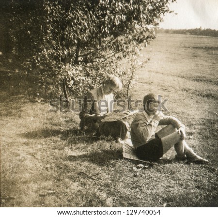 Vintage photo of mother reading a newspaper outdoor and his son, fifties
