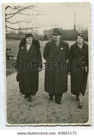 Vintage photo of  parents and daughter walking on the street (thirties)