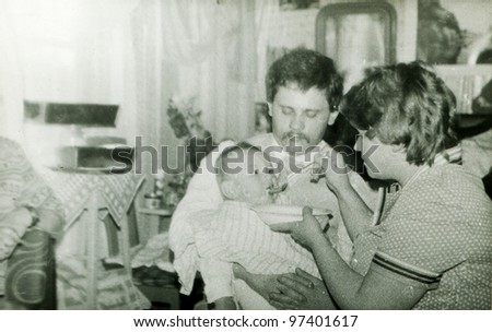 Vintage photo of young parents feeding a baby (early eighties)