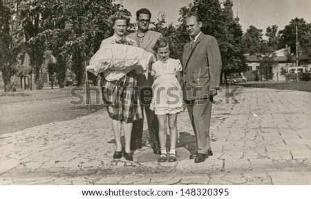 LODZ, POLAND,CIRCA FIFTIES- vintage photo of godparents with a baby in traditional baby\'s sleeping bag for christening, in the company of baby\'s grandfather and sister, Lodz, Poland, circa fifties