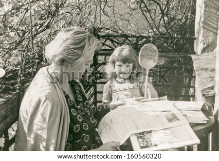 Vintage photo of mother and daughter reading on balcony, sixties