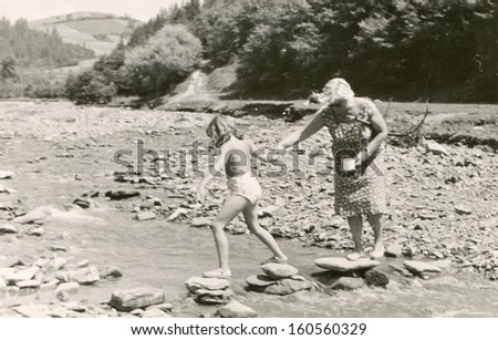 Vintage photo of mother and daughter crossing a river, sixties