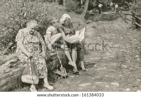 Vintage photo of grandmother, mother and daughter resting on tree trunk and reading