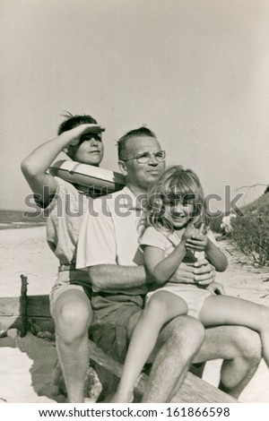 Vintage photo of father playing with children on beach, fifties