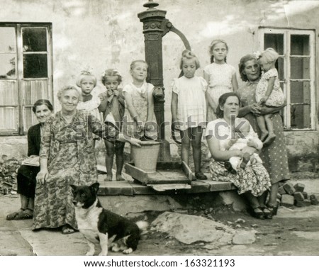 TUREK, POLAND, CIRCA FIFTIES -  unidentified women with children and dog (multigenerational family and neighbors) posing outside, in front of water pump,  - in Turek, Poland, circa fifties