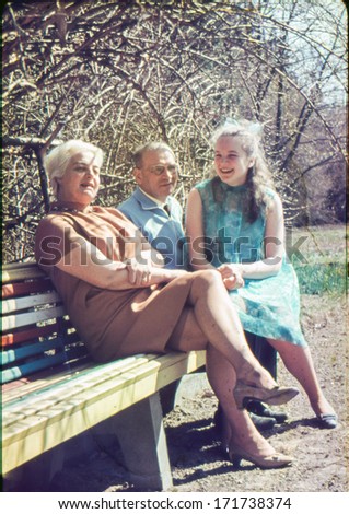 Vintage photo (scanned reversal film) of mature parents with a teenager daughter in garden, sixties