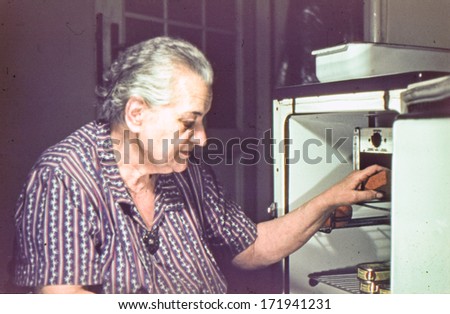 Vintage photo (scanned reversal film) of elderly woman cleaning a fridge, sixties