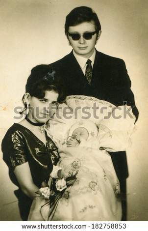 LODZ, POLAND, CIRCA 1970\'s - vintage photo of godparents with a baby in traditional baby\'s sleeping bag for christening