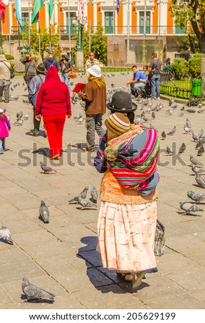 LA PAZ, BOLIVIA, MAY 8, 2014 - Local woman in traditional costume and bowler hat carries her baby in manta shawl on Plaza Murillo