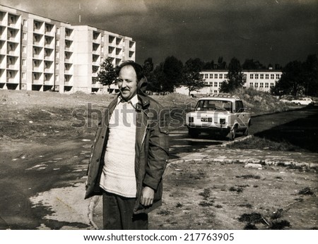 LODZ, POLAND, CIRCA SEVENTIES - Vintage photo of man with modern housing estate and Fiat 125p car in background
