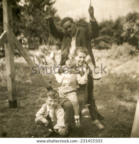 POLAND, CIRCA FIFTIES: Vintage photo of parents with two sons on swing
