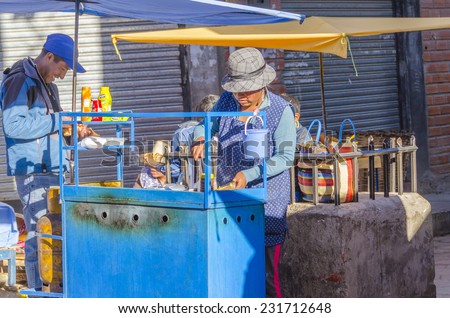 COPACABANA, BOLIVIA, MAY 6, 2014: Local woman in traditional costume and hat sells fast food on street