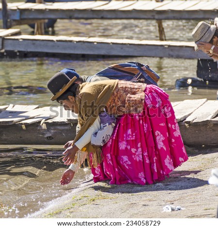 COPACABANA, BOLIVIA, MAY 7, 2014:  Local woman in traditional attire with her husband wash hands in water on jetty in port (Titicaca lake)