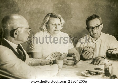 Vintage photo of elderly father playing cards with his adult daughter an son in law, sixties