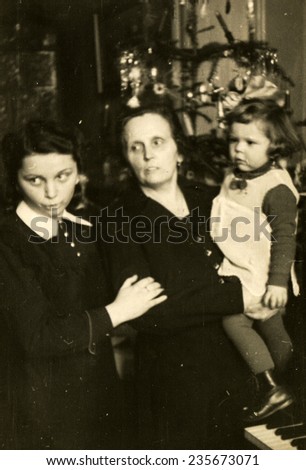 GERMANY, CIRCA 1940s:  Vintage photo of grandmother, mother and little girl in front of Christmas tree