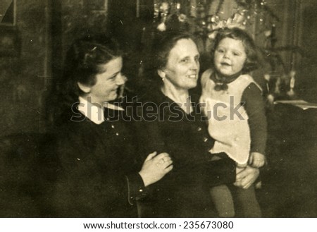 GERMANY, CIRCA 1940s: Vintage photo of grandmother, mother and little girl in front of Christmas tree