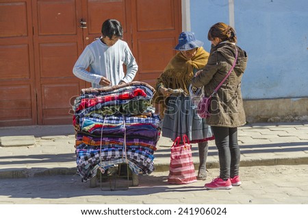 UYUNI, BOLIVIA, MAY 15, 2014:  Local women, one of them in traditional attire, buy blankets from street seller