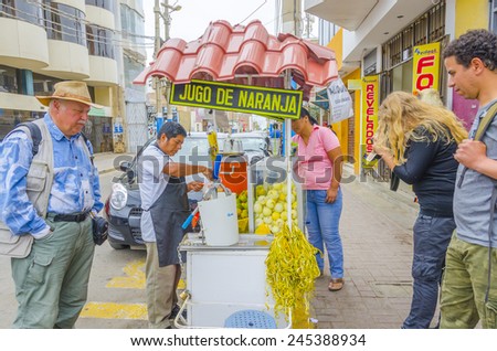 PISCO, PERU, MAY 21, 2014:  Local man prepares fresh orange juice on street stand while tourists wait for drink it