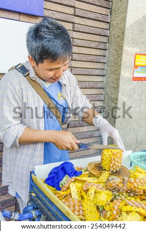 BANGKOK, THAILAND, DECEMBER 26, 2013: Street seller of pineapples peels one of the fruits for buyers