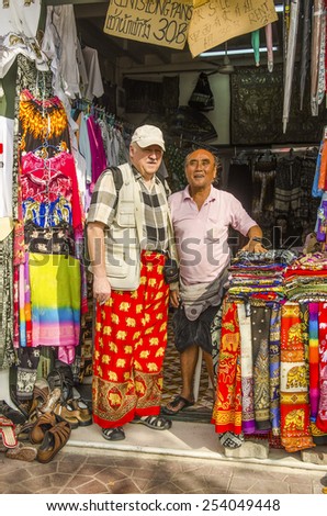 BANGKOK, THAILAND, DECEMBER 26, 2013: Senior tourist poses with the owner of small store selling and hiring clothes suitable for visiting temples