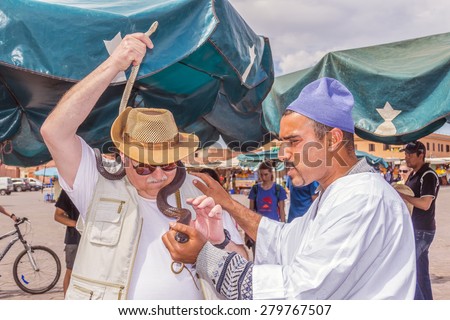 MARRAKESH, MOROCCO, APRIL 3, 2015:  Senior tourist poses for photo with snakes and their owner at Jemaa el-Fnaa square