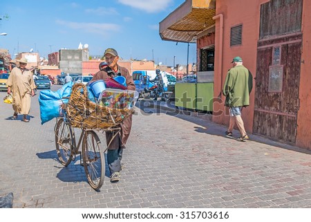 MARRAKESH, MOROCCO, APRIL 16, 2015: Local seller of plastic household items walks in medina transporting his merchandise on bike
