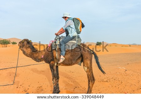 MERZOUGA, MOROCCO, APRIL 13, 2015: young tourist sits on camel, ready for a tour  into the sand dunes of Erg Chebbi