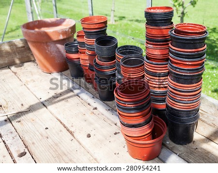 Stacks of dirty plastic flowerpots on a wooden bench in a sunny greenhouse