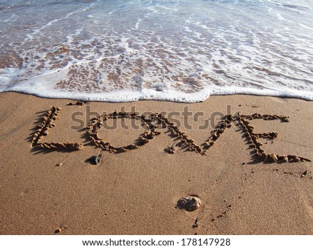 Love written on the sand slowly being washed up by the rising tide